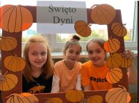 Trzy dziewczynki ubrane na pomarańczowe w ramce z napisem Dzień Dyni.