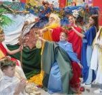 Zdjęcie zawiera żywy obraz Sąd Parysa wykonany przez członków koła dziennikarskiego. Uczennice i uczniowie przebrani w starożytne bóstwa stoją na tle kolorowej dekoracji.