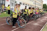 Grupa uczniów na rowerach, ubrani w kamizelki odblaskowe, oczekują na egzamin praktyczny na kartę rowerową